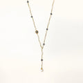 Y-shaped gold-plated necklace with white and gray freshwater pearls on cream background, showing adjustable drop design.