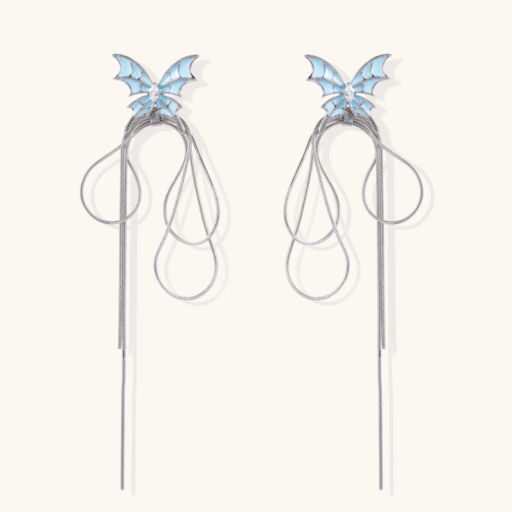 Long silver-tone earrings with powder blue enamel butterfly studs and flowing chain tassels on cream background