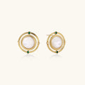 Circular gold stud earrings with iridescent mother-of-pearl center and green zirconia accents on cream background.