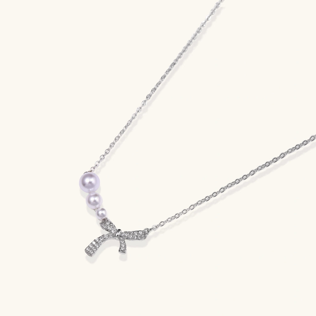 Delicate white gold plated necklace with freshwater pearls and sparkly crystal bow pendant on white background