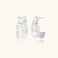 White gold plated sculptural hoop earrings with organic wavy edges and reflective metallic finish on cream background