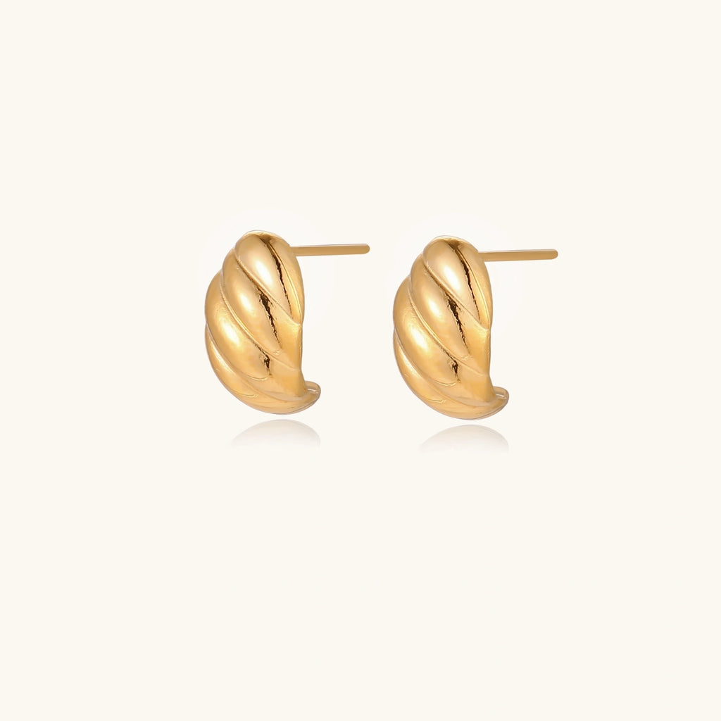 Chunky gold twisted rope huggie hoops with diagonal grooves and high-polish finish on cream background