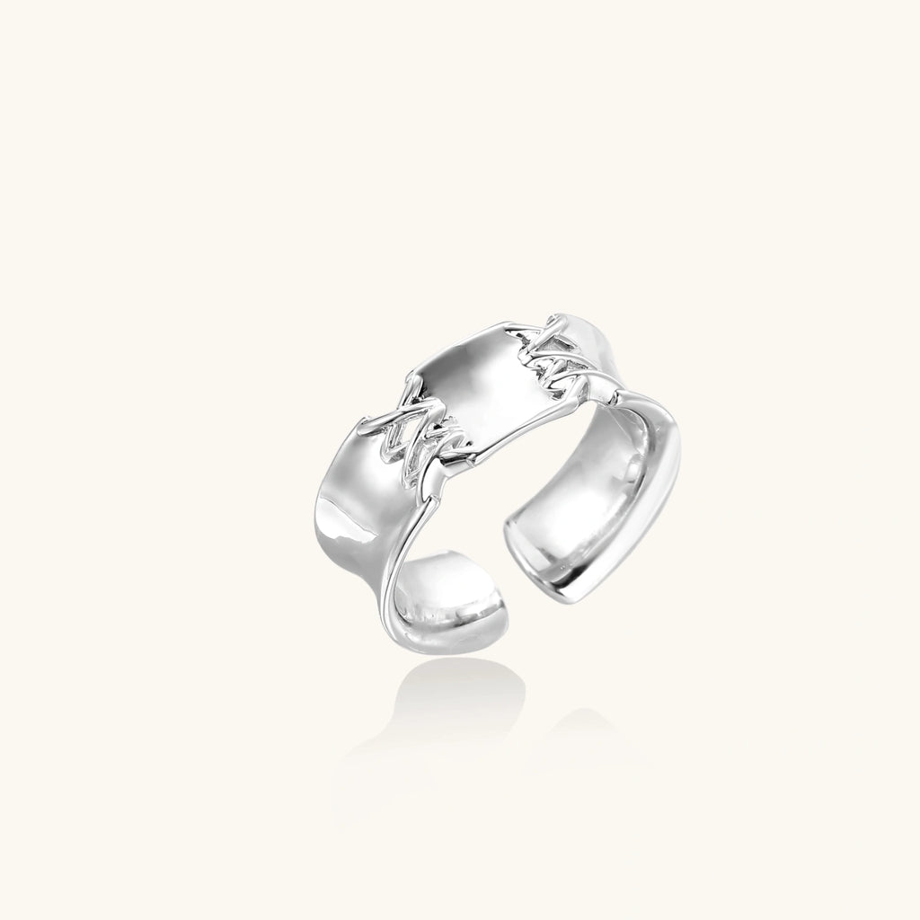 Adjustable silver-toned ring with sculptural stitch design across polished white gold-plated brass band